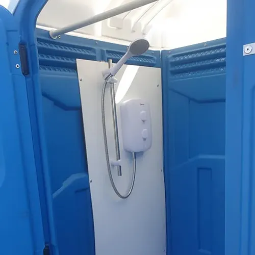 A portable shower unit with blue walls. Inside, there's a showerhead attached to a flexible hose and a control panel on a white panel. The door is slightly open, showing some parts of the interior.